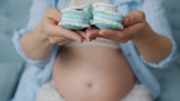 Nahaufnahme einer schwangeren Frau, die Hände streckt und niedliche gestrickte Babystiefel hält — Stockvideo