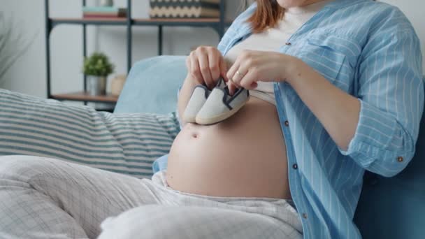 Esperando mãe segurando botas de bebê e andando na barriga se divertindo com a criança em casa — Vídeo de Stock