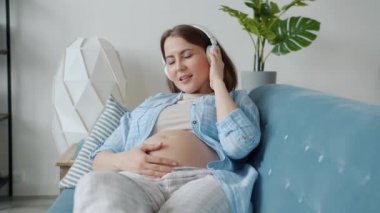 Evde dinlenen kulaklıkla müzik dinleyen hamile bir kadının ağır çekimleri.