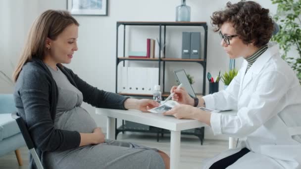 医師と話す妊娠中の患者を見て超音波スキャン画像でテーブルでクリニックオフィス — ストック動画