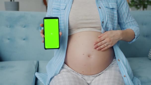 Zbliżenie ciężarnej kobiety trzymającej smartfona z zielonym ekranem chroma key i głaskającym brzuchem — Wideo stockowe
