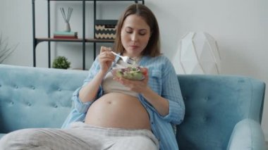 Güzel hamile kadın sebze salatası yiyor evde sağlıklı yemeğin tadını çıkarıyor.