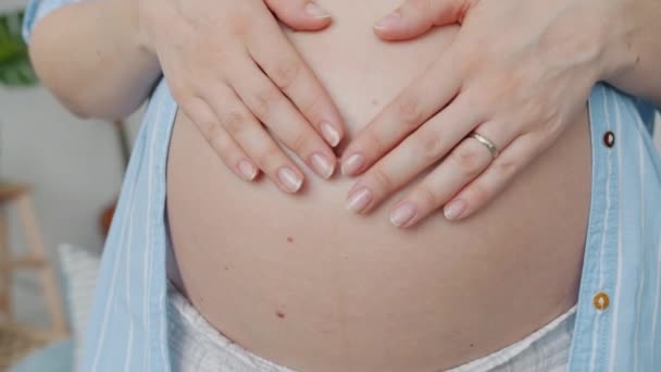 Zbliżenie uroczy ciężarnych kobiet brzuch i dłonie pieszcząc dziecko co symbol serca z palcami — Wideo stockowe