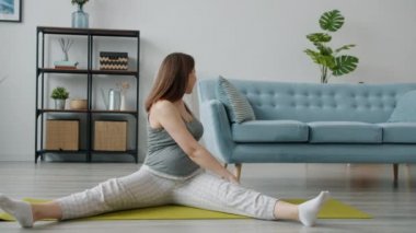 Güzel müstakbel anne oturma odasında yoga minderinde tek başına bacak egzersizi yapıyor.