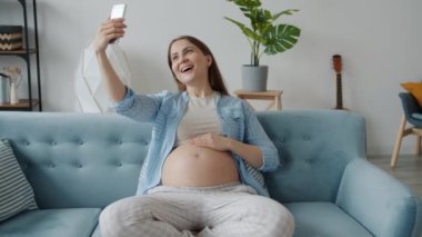 Güzel bir anne beklerken akıllı telefon kamerasıyla evdeki kanepede otururken selfie çekiyor.