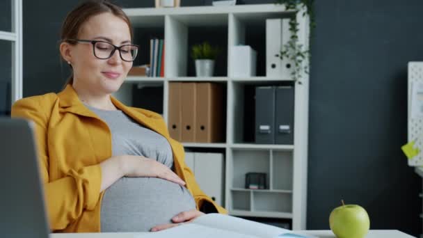 Belle femme enceinte caressant le ventre exprimant le soin et l'amour pour le bébé sur le lieu de travail — Video