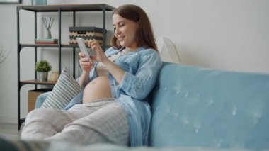 Neşeli bir anne akıllı telefon ekranına dokunuyor. Oturma odasında gülümsemenin keyfini çıkarıyor.