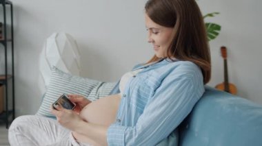 Neşeli hamile kadın akıllı telefon ekranında fetüsün rahme girerken videosunu izliyor.