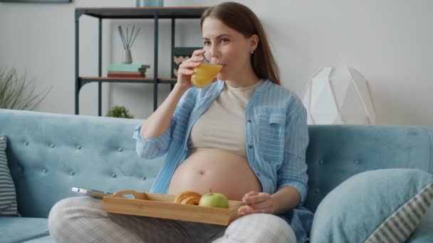 Menina grávida feliz assistindo TV e desfrutar de lanche saudável dentro de casa moderna — Vídeo de Stock