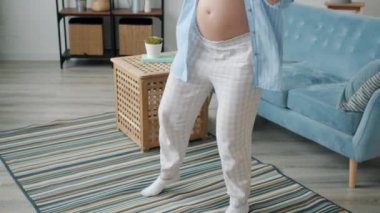 Rahat elbiseli, mutlu ve hamile bir kadının evde dans edip eğlenmesi.