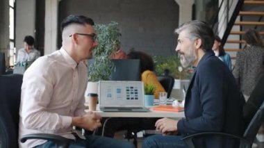 İş adamları konuşuyor, beşlik çakıyor ve gülümsüyor. Akıllı telefon uygulama tasarımıyla dizüstü bilgisayara bakıyor.