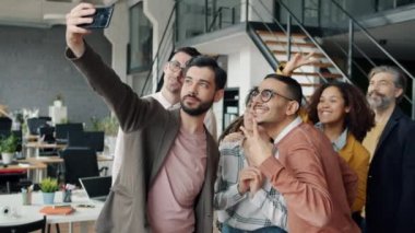 Akıllı telefon kamerasıyla iş ekibiyle selfie çeken genç adam yavaş çekim yapıyor.