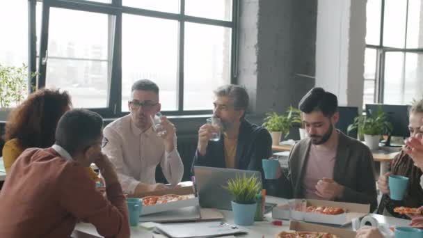 Szczęśliwi pracownicy biurowi jedzący pizzę podczas przerwy w pracy rozmawiający cieszący się jedzeniem razem — Wideo stockowe