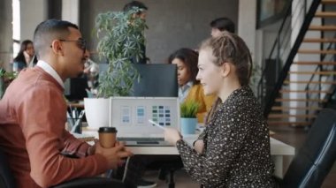 Arap erkek ve beyaz kadın ofiste bilgisayar kullanarak akıllı telefon uygulaması geliştirmeyi tartışıyorlar.