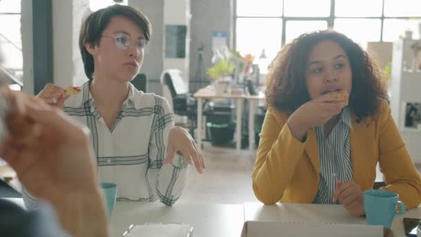 幸せな若い女性白人さんとアフリカ系アメリカ人がオフィスでピザを食べて笑って話しています — ストック動画