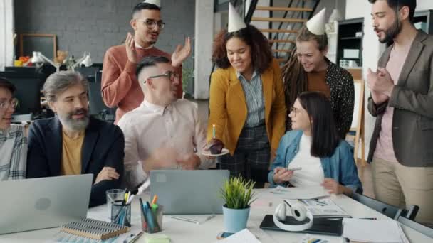 Employees congratulating man on birthday giving cake in office while guy blowing candle making wish — Stock Video