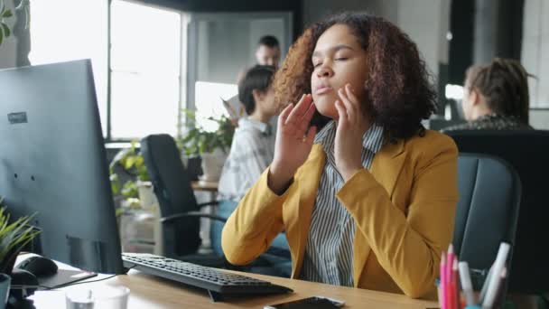 Уставшая афроамериканка касается головы, чувствуя мигрень, работая с компьютером в офисе. — стоковое видео