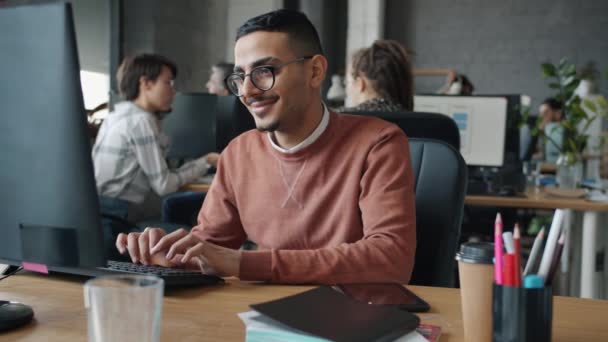 Mouvement lent de l'homme arabe joyeux en utilisant la dactylographie informatique en regardant l'écran au bureau — Video