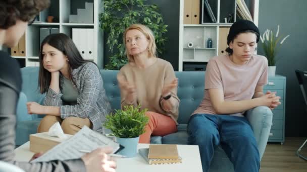 Dojrzała kobieta matka rozmawia z terapeutą podczas gdy nieszczęśliwy nastolatki siedzi na kanapie odwracając się — Wideo stockowe