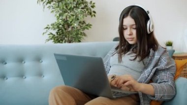 Modern genç, dizüstü bilgisayarla çalışıyor ve kızgın anne geldiğinde kulaklıkla müzik dinliyor.