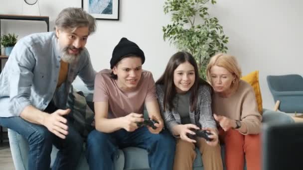Brat i siostra grają w grę wideo w domu, podczas gdy rodzice wiwatują krzycząc śmiejąc się — Wideo stockowe
