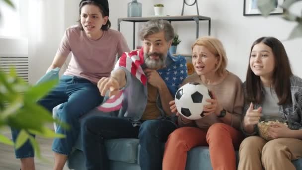 Parents and children enjoying football game on TV cheering doing high-five holding US flag and ball — Stock Video