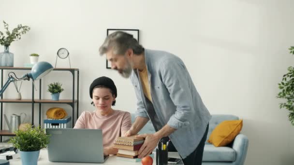 Moderner Teenager benutzt Laptop, wenn Vater Bücher mitbringt und Computer mitnimmt — Stockvideo