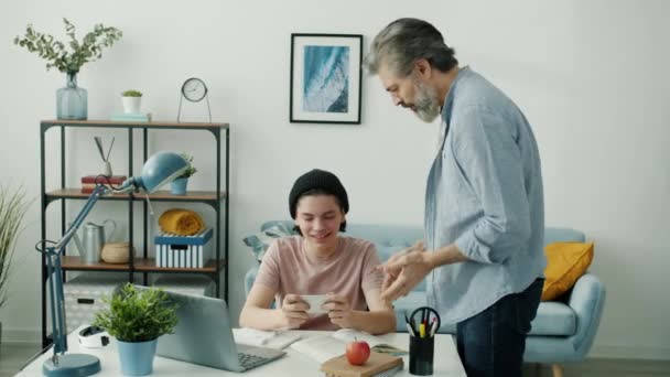 Father scolding teenager for playing with smartphone making him do homework in apartment — Stock Video