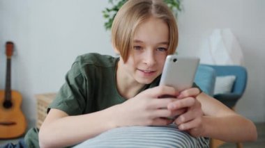 Akıllı telefon kullanan, ekranlara dokunan ve evde gülümseyen mutlu genç bir çocuk.