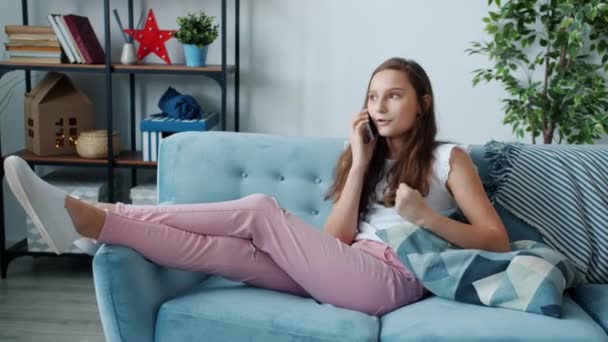 Adolescente emocional disfrutando de la conversación en el teléfono móvil relajándose en el sofá en la sala de estar — Vídeo de stock