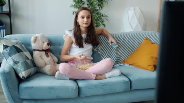 Gondtalan tinédzser lány TV-t néz és popcornt eszik egyedül pihen a lakásban — Stock videók