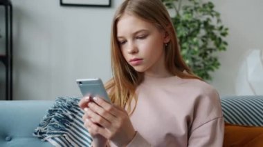 Apartmanda kanepede oturmuş akıllı telefon mesajları kullanan ciddi bir genç kız.