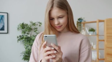 Evde akıllı telefon dokunuşu ekranı kullanan mutlu genç kızın yavaş çekimde portresi.