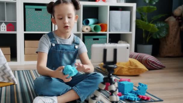 Χαριτωμένο μικρό κορίτσι blogger καταγραφή βίντεο για την μοντελοποίηση πηλό μιλάμε για κάμερα smartphone δείχνει αντίχειρες-up — Αρχείο Βίντεο