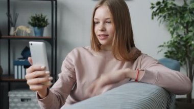 Akıllı telefon kullanan mutlu genç kız çevrimiçi video görüşmesi yapıyor, konuşuyor ve evden el sallıyor.
