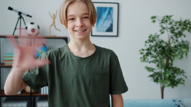 Powolny portret przystojnego nastolatka machającego ręką i uśmiechającego się stojącego w domu — Wideo stockowe