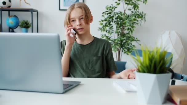 Cep telefonuyla konuşan mutlu çocuğun iyi haberleri kutlaması ve evde dizüstü bilgisayar kullanması. — Stok video