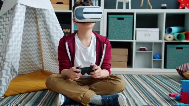 Pojke bär virtuella verklighets glasögon spela TV-spel med hjälp av styrenhet och titta runt att ha kul ensam — Stockvideo