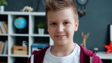 Modern, rahat bir odada kameraya bakıp gülümseyen neşeli bir çocuğun yakın plan portresi.