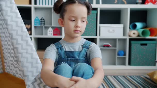 Smutny dzieciak siedzi na podłodze z nieszczęśliwą obojętną twarzą ignorując zabawki w przytulnym pokoju — Wideo stockowe