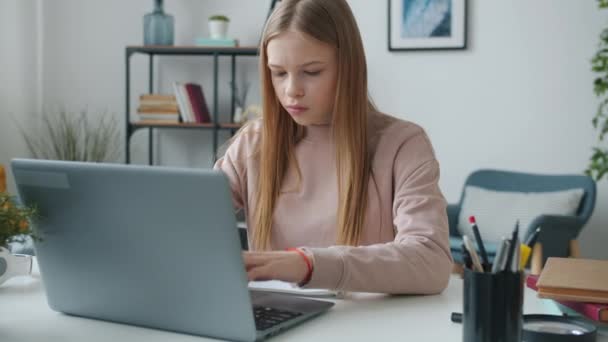 Серйозна дівчина-підліток використовує ноутбук, а потім робить нотатки в книзі, що навчається вдома — стокове відео