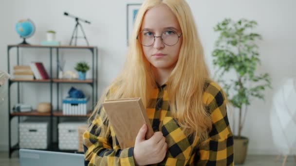 Портрет повільного руху серйозного підлітка, що стоїть вдома, тримає книгу зворушливі окуляри — стокове відео