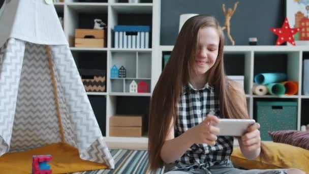 Excited kid playing smartphone video game touching screen and smiling sitting on floor at home — Stock Video