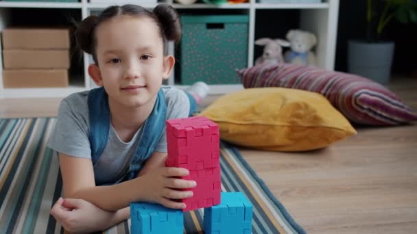 Retrato em câmera lenta de uma criança adorável segurando brinquedos no chão e olhando para a câmera — Vídeo de Stock