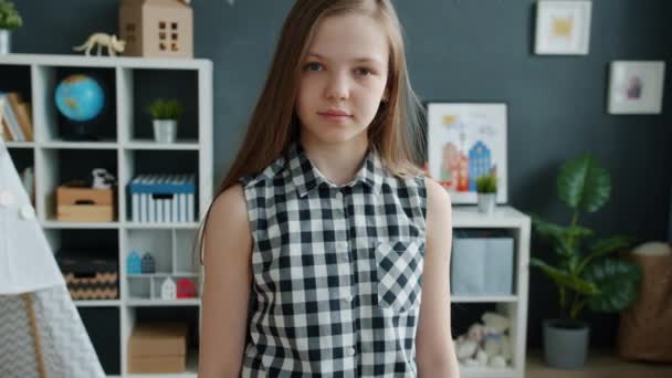 Portret van slim kind meisje kijken naar camera met licht glimlach staan alleen in huis — Stockvideo