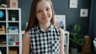 Rahat bir odada kameraya bakarak gülümseyen neşeli kızın ağır çekim portresi.