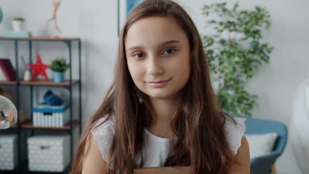 Portrait of cute young lady holding book smiling at camera indoors in cozy house — Stok Video