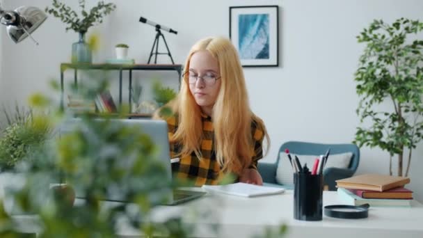 Ragazzo serio che fa i compiti a casa lavorando con il computer e scrivendo nel quaderno in appartamento — Video Stock