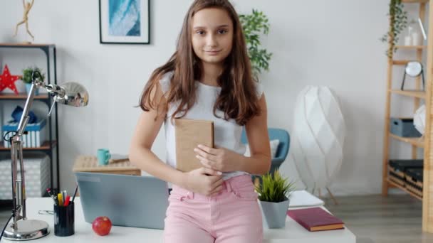 Slow motion porträtt av attraktiv tonåring flicka står hemma håller bok och ler — Stockvideo
