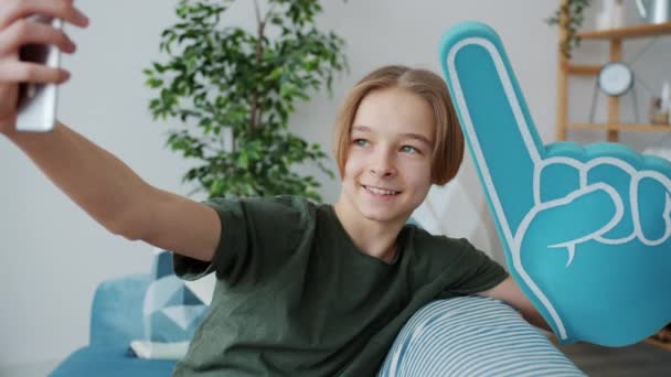 Niño creativo tomando selfie en casa posando con gran mano de espuma sonriendo usando la cámara del teléfono inteligente — Vídeos de Stock